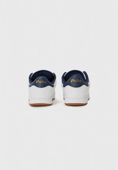 Baskets blanches avec une finition lisse et des accents bleu marine. Comprend un col rembourré, une semelle en caoutchouc et un logo "Polo" en or sur le talon.