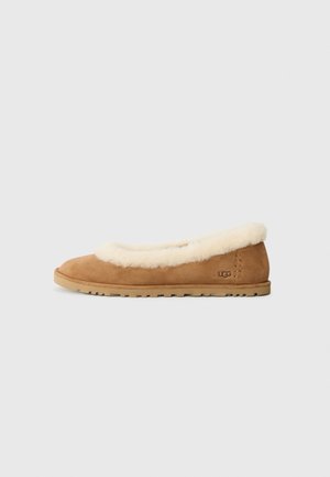 Chausson plat en daim beige avec doublure en fourrure crème et semelle en caoutchouc, logo UGG embossé sur le côté du talon.