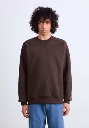 Brown sweatshirt with a crew neck, raglan sleeves, and ribbed cuffs. Notable detail includes a small logo tag on the left sleeve.
