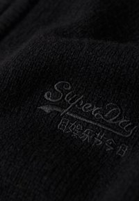 Tessuto nero a maglia con logo "Superdry" in rilievo, dalla consistenza morbida e con motivo a coste.