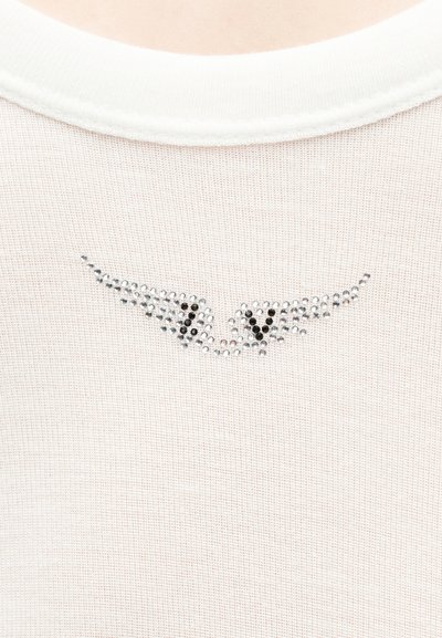 Λευκό πλεκτό ύφασμα με διακοσμητικά στρας που σχηματίζουν ένα στυλιζαρισμένο, αφηρημένο ζευγάρι ματιών κοντά στη γραμμή του λαιμού.