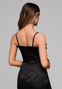 Černé saténové šaty s tenkými ramínky a přiléhavým trupem. Mají hladkou texturu a jemný tečkovaný vzor, se skrytým zipem na zadní straně.