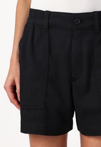 Černé bavlněné šortky s elastickým pasem a zapínáním na knoflík, vybavené postranními kapsami a uvolněným střihem. Hladká textura a lemované okraje.