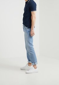 Camisa polo navy con ribete blanco, combinada con jeans de puño enrollado azul claro y zapatillas blancas. Atuendo casual con un diseño clásico y líneas limpias.