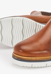 Brown leather ankle boots with a smooth texture, rounded toe, and white rubber sole featuring a wavy pattern. Blue accent at sole edge.
