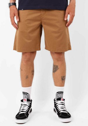 Shorts en tissu marron, coupe droite, au-dessus du genou. Associés à des baskets montantes noires et des chaussettes blanches ornées de détails graphiques.