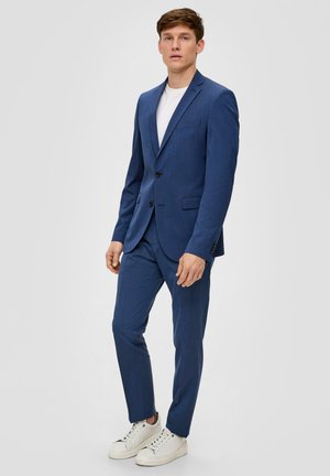 Marineblaues Sakko mit zwei Knöpfen, Reverskragen und passender Hose. Getragen über einem weißen Hemd und kombiniert mit weißen Sneakers.