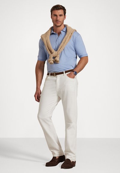 Ανοιχτό μπλε πόλο μπλουζάκι με μια μπεζ πλεκτή ζακέτα πεταμένη στους ώμους, λευκά παντελόνια και καφέ σουέτ μοκασίνια, εφοδιασμένα με δερμάτινη ζώνη.