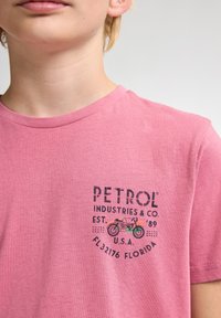 Lyserød bomulds T-shirt med rund hals og korte ærmer, prydet med et grafisk design af en motorcykel og brandtekst på brystet.