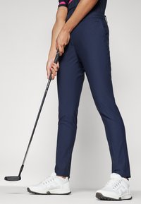 Námořnické golfové kalhoty v přiléhavém střihu s hladkým povrchem. V páru s bílými sportovními botami s šedými akcenty a texturovanou podrážkou.