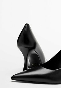Escarpins à talons hauts en cuir noir avec un bout pointu et un talon aiguille fin. Texture lisse et design minimaliste, avec une silhouette courbée.