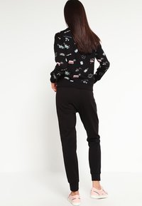 Svart sweatshirt med färgglada grafiska mönster, parat med svarta joggers. Outfiten har ribbade ärmslut och en avslappnad silhuett.