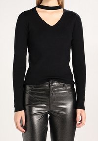 Svart långärmad tröja med V-ringning och en utskärning vid kragen, matchad med blanka svarta metallicbyxor.