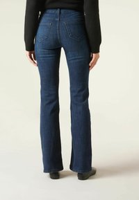 Vaqueros acampanados azul oscuro con tiro medio y diseño de cinco bolsillos, que presentan sutiles detalles de costura y una textura de denim suave.