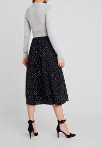 Gray long-sleeve cropped sweater paired with a black polka dot midi skirt and black high-heeled shoes with an ankle strap.