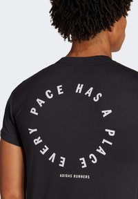 Svart t-shirt med korta ärmar, tillverkad av mjukt tyg, med vit cirkulär textdesign på baksidan som säger "VARJE TEMPO HAR SIN PLATS."