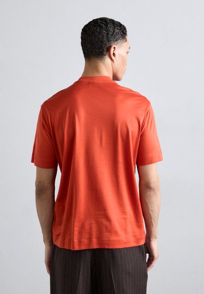 Trumpas rankovės, apvaliai iškirptas marškinėliai ryškiai oranžinės spalvos, pagaminti iš lygaus medvilnės mišinio, pasižymi laisvu kirpimu ir subtiliais siuvinėjimo akcentais.