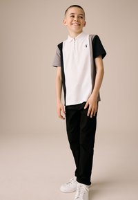 Rövid ujjú galléros póló fehér, szürke és fekete anyagból; cipzáras gallérral, színblokk dizájnnal, fekete nadrággal és fehér tornacipővel párosítva.