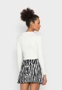 Top de manga longa branco canelado combinado com uma saia mini de padrão zebra preto e branco, com um detalhe de laço na cintura.
