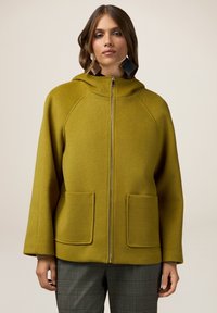 Giacca a vento olive green in tessuto texturizzato, con zip a tutta lunghezza, due tasche frontali e una vestibilità rilassata.