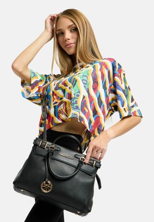 Schwarze Ledertasche mit strukturierter Form, goldenen Hardware-Details und texturiertem Oberflächenfinish. Das Model trägt ein lebhaftes, mehrfarbiges, abstrakt bedrucktes Oberteil.