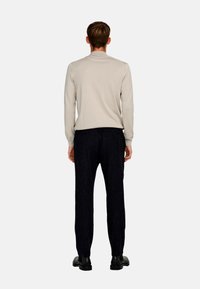 Light beige sweater with a ribbed texture, long sleeves, and a high neckline paired with dark tailored pants and black shoes.