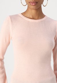 Maglia rosa chiaro a maniche lunghe con scollo rotondo e silhouette aderente. La texture è morbida, con righe verticali in tutto il capo.
