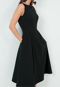 Černé bezramínkové šaty s přiléhavým korzetem, rozšířenou sukní, bočními kapsami a jemnými sklady. Vyrobené z hladkého materiálu, minimalistický design.