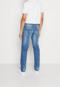 Vaqueros de mezclilla azul con corte de pierna recta, dos bolsillos traseros y un acabado ligeramente desteñido, combinados con una camisa blanca de manga corta.