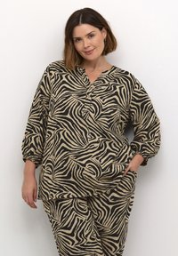 Set pohodlného oblečenia so zebrovým vzorom v béžovej a čiernej farbe, obsahujúci vrch s uvoľneným strihom, gombíkmi a elastickými manžetami, spárovaný s rovnakými spodkami.