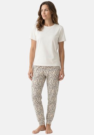 Femme debout pieds nus, portant un t-shirt blanc uni à manches courtes et un pantalon de jogging clair à motif floral.