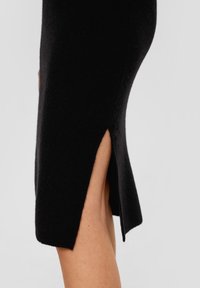 Svart stickad klänning med en figurnära silhuett, med detaljer som en sidoklyvning och ribbad textur i fållen. Slät, varm tyg.