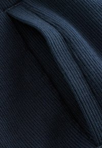 Tamsiai mėlynos spalvos ribuota megzta medžiaga, sulankstyta taip, kad išryškėtų tekstūra ir pynimo raštas iš arti.