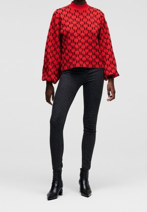 Pull rouge avec motif logo noir, manches ballons et col rond. Assorti avec un jean noir ajusté présentant un motif subtil. Bottines noires.