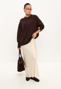 Pulover oversized tricotat de culoare maronie, fustă din satin crem, geantă din suede maron închis și încălțăminte. Design simplu, croială lejeră și texturi netede.