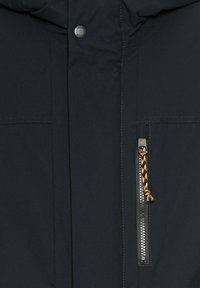 Marine Parka mit glatter Textur, ausgestattet mit einem Reißverschluss mit einem orange-schwarzen Zugband, Metall-Druckknöpfen und zwei Fronttaschen.