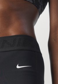 Närbild av en persons vältrimmade midja iförd svarta Nike leggings med en vit Nike swoosh-logga på höften och en matchande sport-BH.