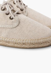 Scarpe in canvas beige chiaro con superficie strutturata, punta rotonda e cuciture in tonalità cremoso. Presentano una suola in corda di juta e chiusura con lacci.