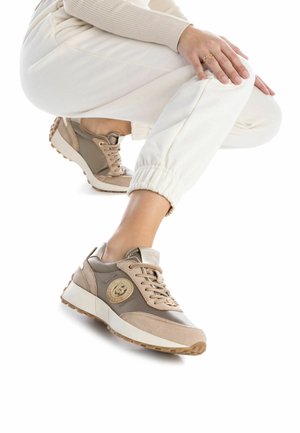 Zapatillas beige y marrones con un diseño de ante y cuero, presentando un acento de logo redondo y una suela de goma texturizada.