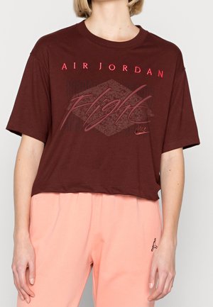 Kobieta nosząca krótki, ciemnoczerwony T-shirt Air Jordan z napisem „Flight” oraz jasnoróżowe spodnie z małym logo Jordan.