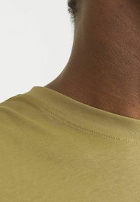 Oliven grøn bomuld T-shirt med rund halsudskæring og blød tekstur, med synlige sting langs kraven og skulderen.