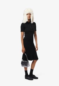 Polo texturizado negro de manga corta, falda midi negra, calcetines negros, zapatillas negras y un bolso acolchado brillante. Gorra blanca forrada de piel.
