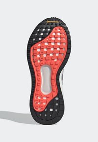 Semelle de chaussure avec une bande de roulement noire et orange, une semelle intermédiaire blanche visible à travers des trous, et un logo Continental près de la zone des orteils.