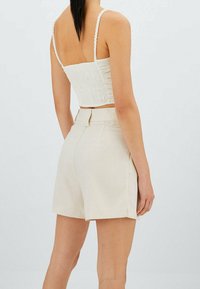 Haut court blanc avec une texture froncée et des bretelles fines, associé à un short beige taille haute. Le tissu a une finition lisse et légère.