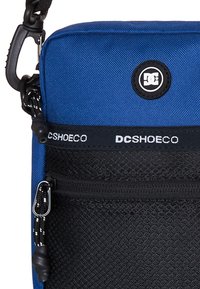 Blauwe stoffen schoudertas met een zwart mesh voorvak, rits en DC Shoes logo. Beschikt over een afneembare schouderband en een gestructureerde afwerking.