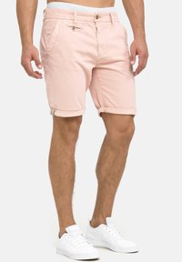 Shorts en coton rose clair avec des ourlets roulés, poches avant et fermeture à bouton. Associés à des baskets blanches, avec lacets et un design minimaliste.