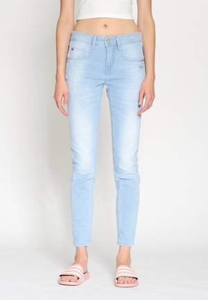 Light blue skinny jeans made of denim with a faded finish, featuring front pockets, a zip fly, and a fitted silhouette. Paired with pink slide sandals.