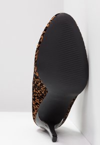 Chaussure à talon haut à bouts pointus à imprimé léopard montrée par la semelle avec un dessous texturé noir et un talon fin sur fond blanc.