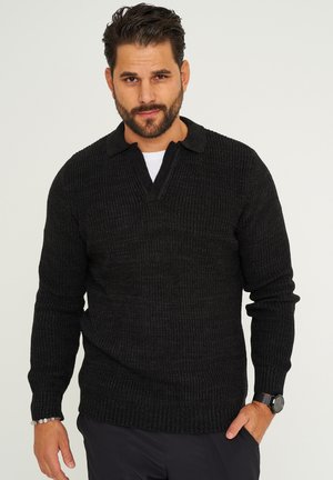 Schwarzer gestrickter Pullover mit V-Ausschnitt und kurzem Kragen. Verfügt über eine gerippte Textur und lange Ärmel. Über einem weißen Hemd getragen, präsentiert das Modell einen lässigen Look.