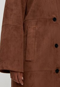 Bruine faux-suède jas met een getextureerde afwerking, voorzien van een enkele zwarte knoop, ruime mouwen en een zijzak.